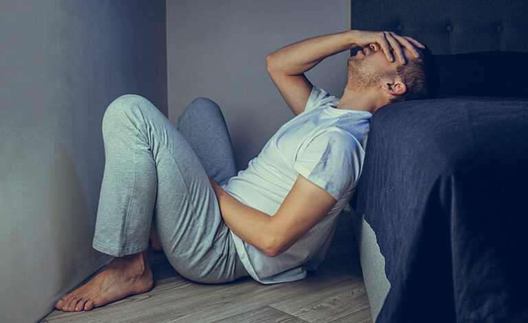 Man suffering with depression sat at the side of his bed