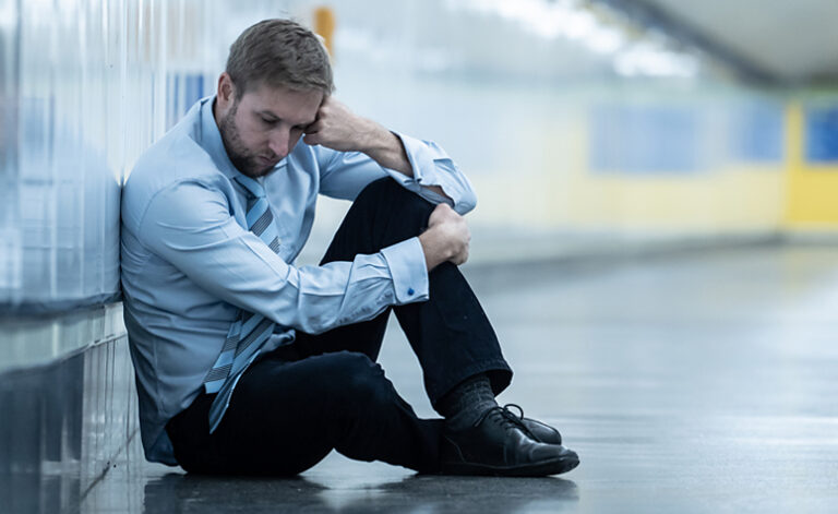 Man suffering from fatigue sat on train tube floor with depression