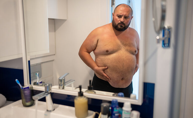 Depressed obese man looking at his body in the mirror seeking to change his lifestyle