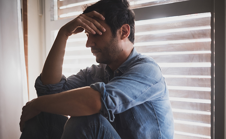 Depressed man sat by window contemplating life