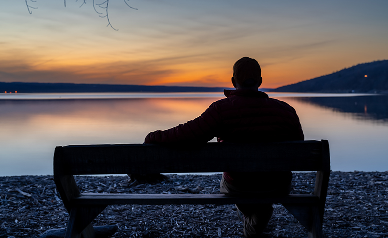 Man looking out over a sunset lake contemplating life