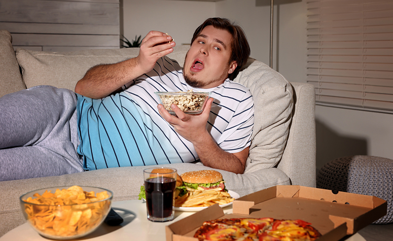 Man sat on sofa with over eating disorder, gorging on fast food