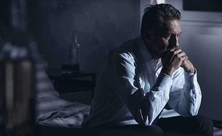 Man with alcohol addiction sat on bed frustrated and depressed