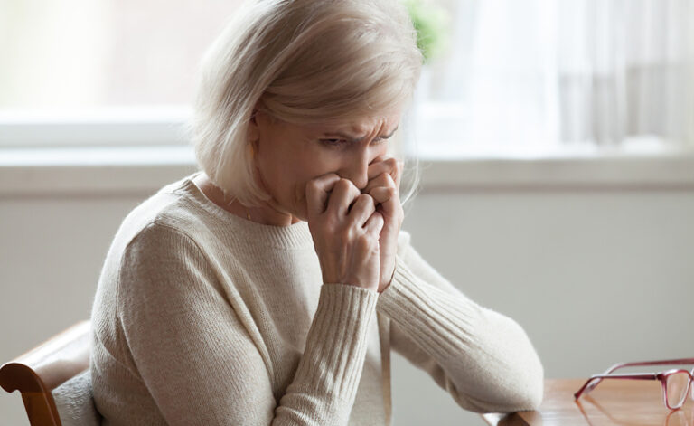 Older lady sat at table sad with low self-esteem due to depression