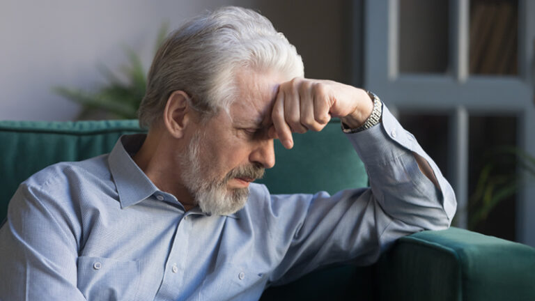 Older man sat of sofa suffering with symptoms of anxiety