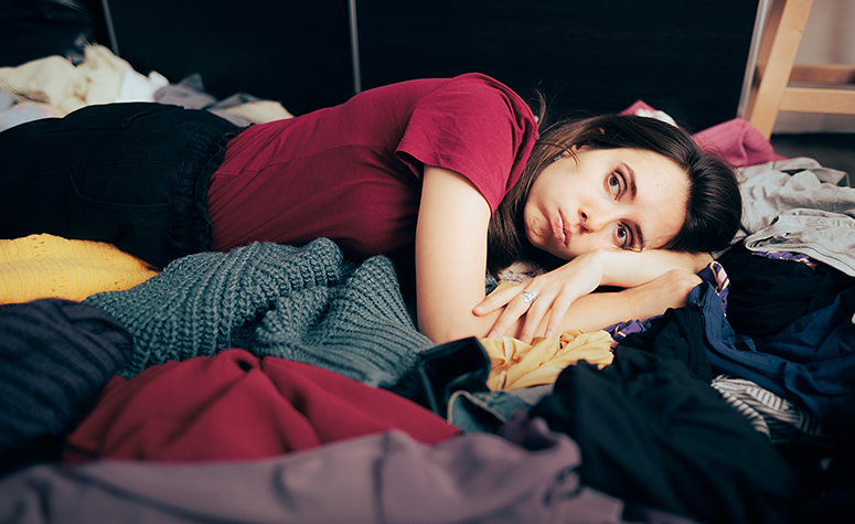 Shopping addict laid on the bed depressed and surrounded by many clothes