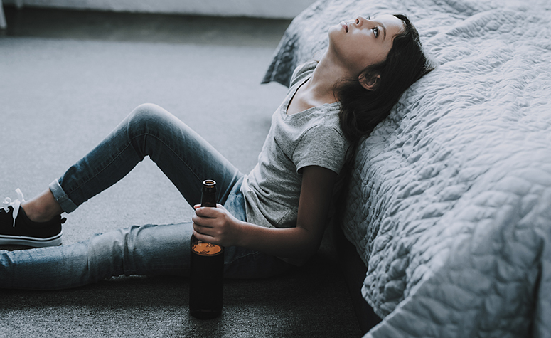 Woman sad and drinking alcohol sat by the side of the bed