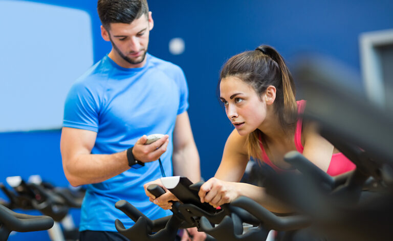 Woman exercising hard in the gym on a bike, demonstrating symptoms of exercise addiction