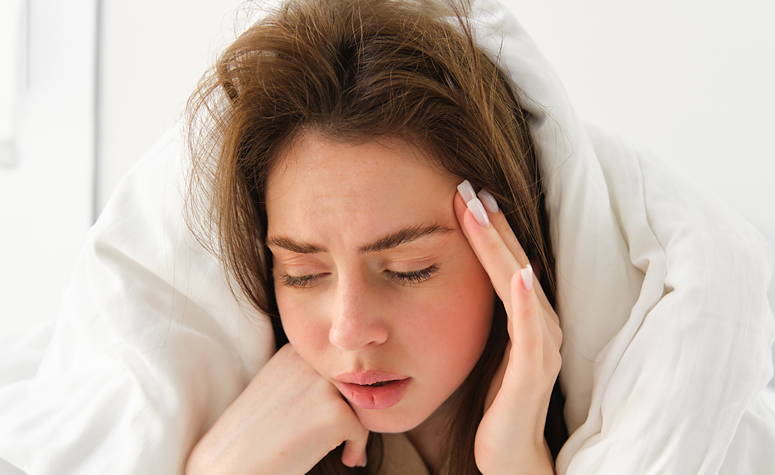 Woman in bed suffering with a hangover after drinking too much alcohol