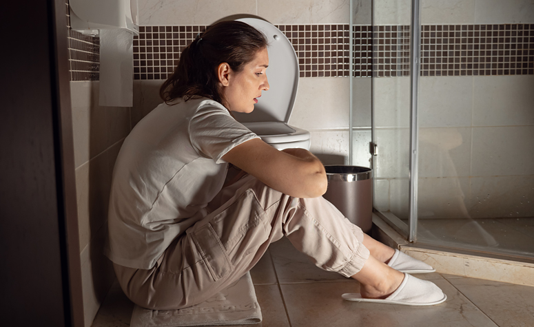 Women suffering from severe hangover sat on bathroom floor by the toilet