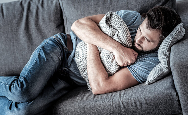 Man suffering with somatic syndrome symptoms laid on sofa fatigued