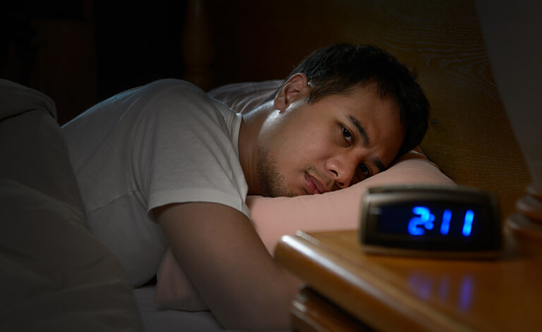 Man laid awake suffering from insomnia looking at the clock