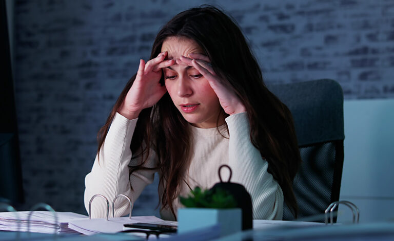 Woman suffering with symptoms of stress whilst sat at her desk
