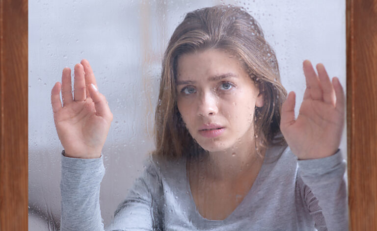 Woman with SAD looking gloomily out of the window at the rain