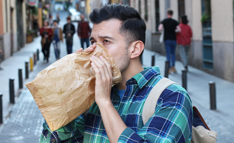 Man suffering with anxiety blowing into a paper bag to help regulate his breathing and reduce the symptoms of anxiety